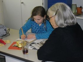 Zeitzeugin beim Erzählen: ein junges Mädchen und eine alte Frau sitzen gemeinsam an einem Tisch. Foto: Stadt Oldenburg