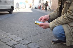 Ein hockender Mann mit einem digitalen Gerät dokumentiert einen Straßenschaden. Foto: Stadt Oldenburg