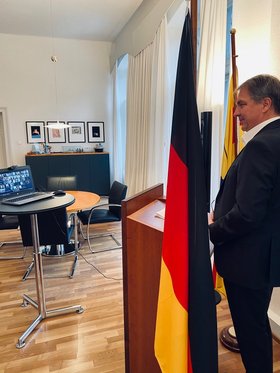 Oberbürgermeister Krogmann an einem Rednerpult, die Teilnehmenden aus den Partnerkommunen sind digital zugeschaltet, ein Laptop steht auf einem Tisch vor Herrn Krogmann. Foto: Stadt Oldenburg