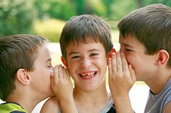 Zwei Jungs flüstern einem anderen Jungen etwas ins Ohr. Foto: Sonya Etchison/Fotolia