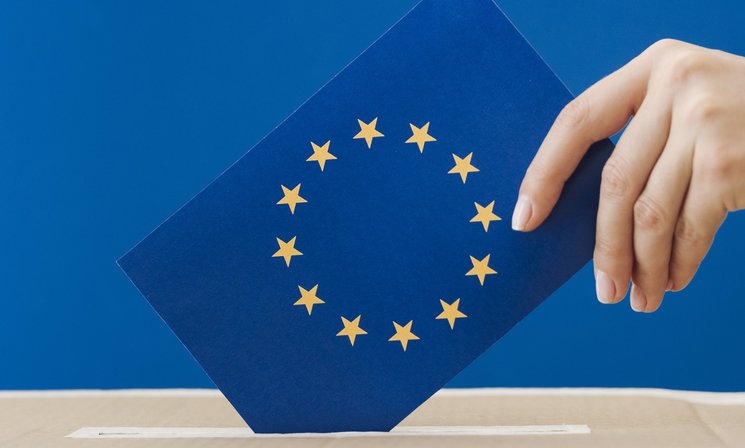 Hand steckt Europaflagge in eine Wahlurne. Foto: Freepik
