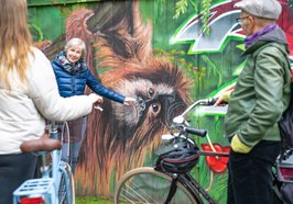 Eine Gästeführerin und Teilnehmende stehen vor einem Graffiti mit einem Affen. Foto: OTM/Mario Dirks