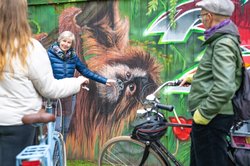 Eine Gästeführerin und Teilnehmende stehen vor einem Graffiti mit einem Affen. Foto: OTM/Mario Dirks