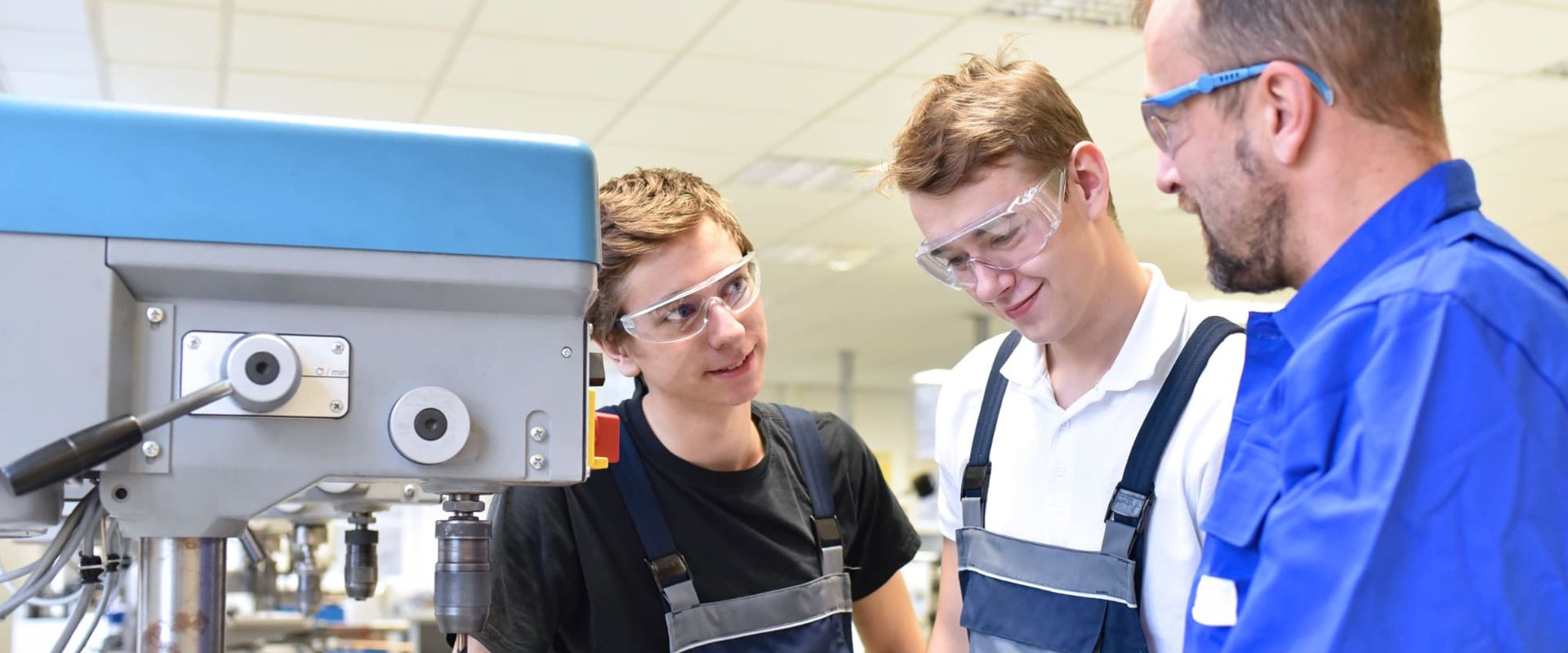 Zwei Auszubildende erhalten in einer Metallbauer-Werkstatt eine Geräteeinweisung von ihrem Ausbilder. Foto: stafftastic