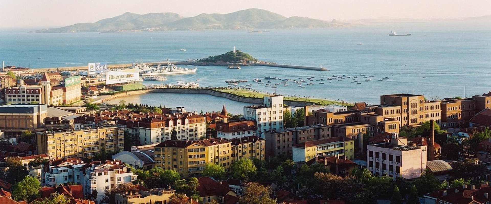 Luftbild, im Vordergrund sind Gebäude zu erkennen, im Hintergrund das Meer und eine bergige Insel. Foto: Stadt Qingdao