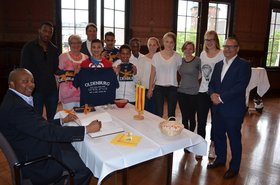Winston Adam Gugulethu, Sportministerium Eastern Cape, trägt sich ins Gästebuch der Stadt ein. Im Kreis im den Tisch stehen Triathletinnen und Triathleten aus Südafrika und Deutschland. Foto: Stadt Oldenburg