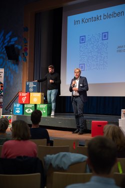 Zuschauerinnen und Zuschauer hören Redner auf der Bühne zu. Foto: Grafikstudio17