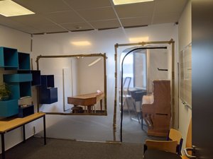 Präparierter Raum für Unterricht mit Blasinstrumenten und Gesang. Foto: Stadt Oldenburg Ein durchsichtige Folie teilt einen Raum in zwei Hälften. Im vorderen Teil hängt ein blaues regal, im hinteren sind ein Klavier sowie ein Cembalo sichtbar.