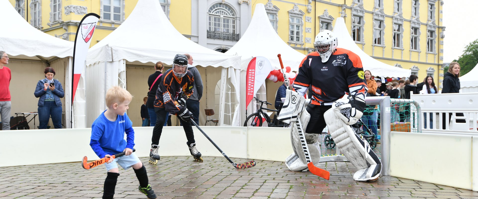 Ein kleiner Junge und zwei Erwachsene in voller Montur spielen Hockey. Foto: Tobias Frick