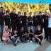 Vorschau: Gruppenfoto, in der vorderen Reihe sitzen einige Personen auf dem Boden, alle tragen schwarze T-Shirts mit dem gleichen Logo. Foto: Edna Taff