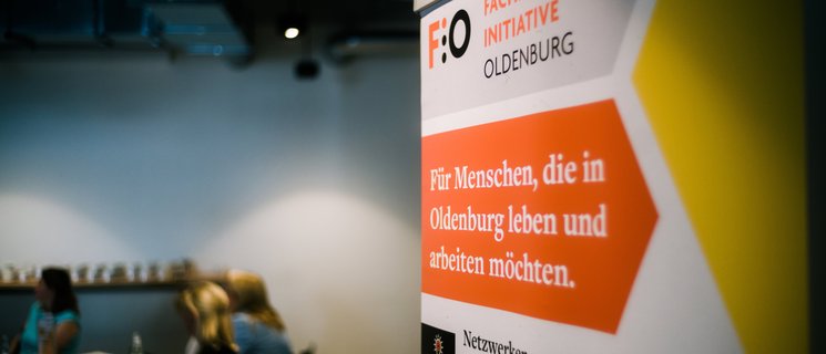 Roll-up der Fachkräfte-Initiative Oldenburg, im Hintergrund Gruppenarbeitsphase während eines Fachkräfte-Forums. Foto: Jörn Tempel