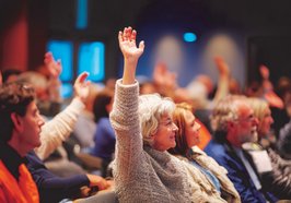 Menschen auf einer Versammlung, eine Seniorin meldet sich. Foto: GoshaMovies/AdobeStock