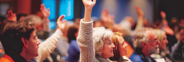 Menschen auf einer Versammlung, eine Seniorin meldet sich. Foto: GoshaMovies/AdobeStock