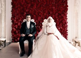 Hochzeitsbild der Protagonistin Aynur: Das Ehepaar sitzt auf zwei Stühlen vor einer Wand aus roten Rosen und sieht mit ausdrucksloser Mine in die Kamera. Foto:  Hochzeitsbild der Protagonistin Aynur: Das Ehepaar sitzt auf zwei Stühlen vor einer Wand aus roten Rosen und sieht mit ausdrucksloser Mine in die Kamera. Foto: NFP marketing & distibution GmbH