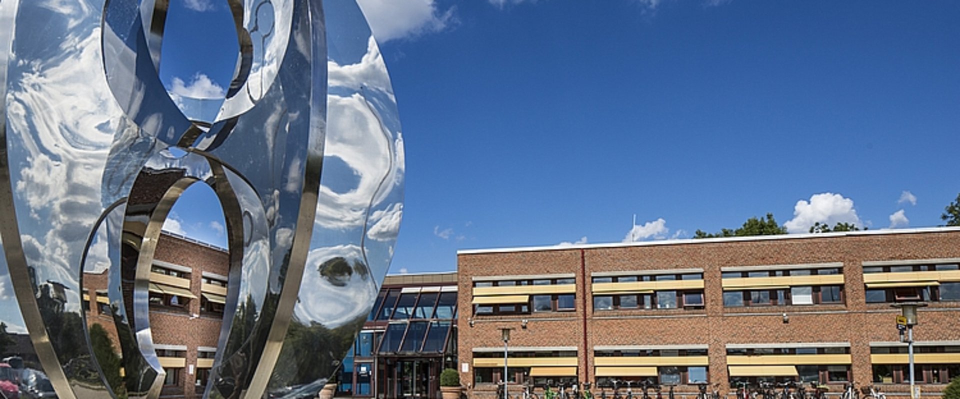 Skulptur aus spiegelndem Metall, im Hintergrund das Backsteingebäude des Rathauses von Høje-Taastrup. Foto: Claus Björn Larsen