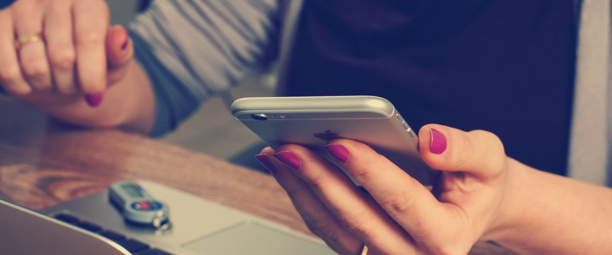 Frau an einem Laptop mit einem Smartphone in der Hand. Foto: Pexels.com