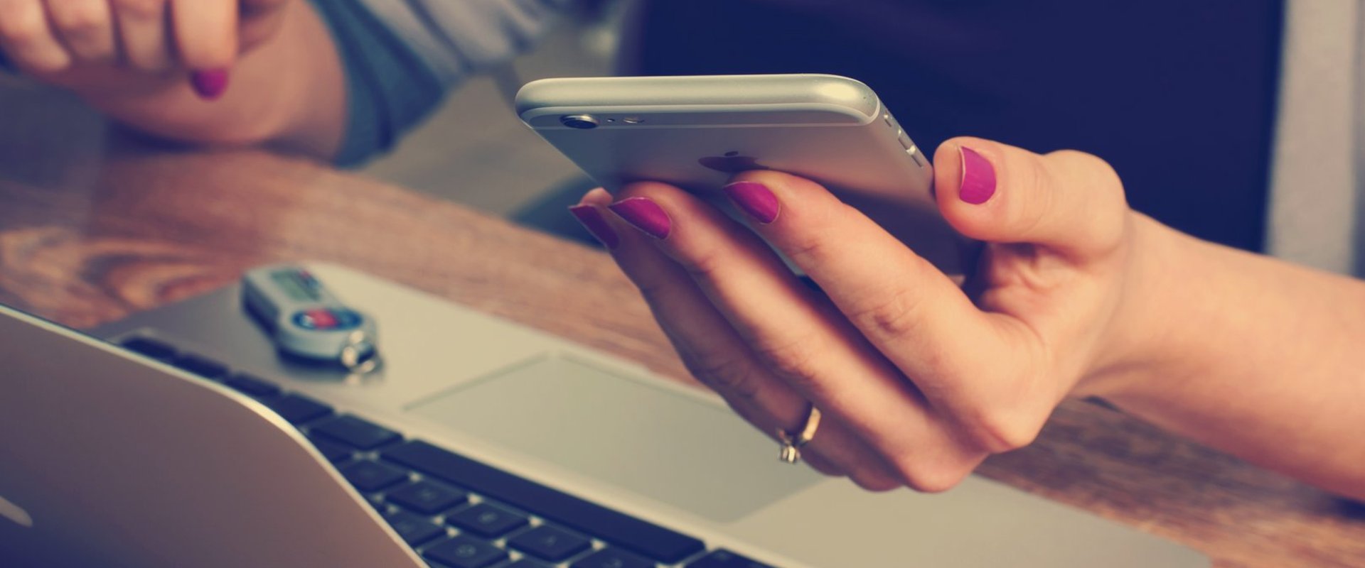 Frau an einem Laptop mit einem Smartphone in der Hand. Foto: Pexels.com