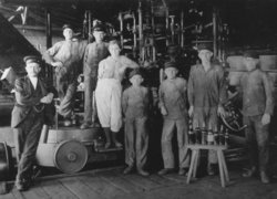 Arbeiterinnen und Arbeiter in der Oldenburgischen Glashütte vor einer der ersten Flaschenblasmaschine, um 1917. Quelle: Stadtmuseum
