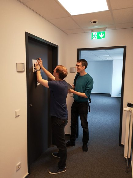 Holger Denckmann und Philipp Schlüchtermann bringen Raumnummern zur Orientierung für das Umzugsunternehmen an. Foto: Stadt Oldenburg