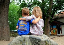 Zwei Kinder sitzen Arm in Arm auf einem Stein. Foto: S.v.Gehren/pixelio.de