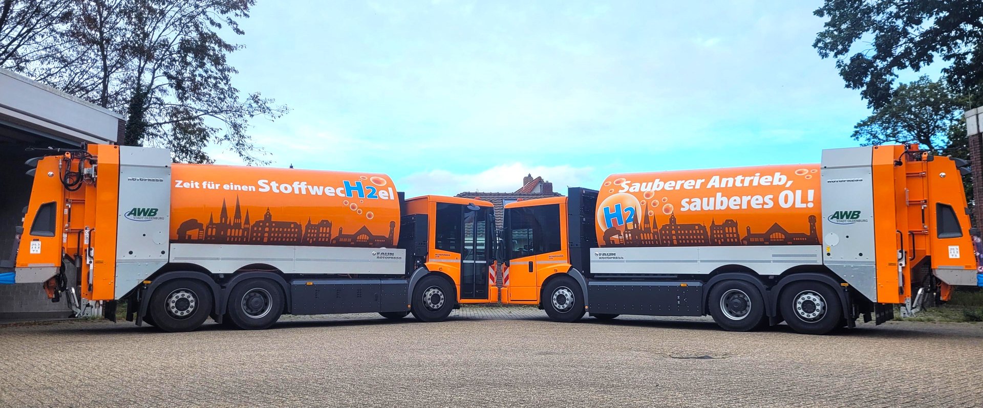 Die beiden wasserstoffbetriebenen Sammelfahrzeuge des AWB stehen Front an Front zusammen. Ein Wagen trägt den Spruch "Zeit für einen Stoffwechsel", der andere "Sauberer Antrieb, sauberes OL!". Foto: Stadt Oldenburg