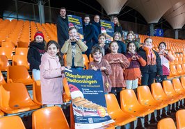 Freuen sich auf das Stadionsingen: (hinten, von links) Marco Harms (Sportbüro der Stadt Oldenburg), Dimitri Melnik (Leiter der Musikschule), Christian Köhler (Vorsitzender der Regionalen Stiftung der LzO) und Chantal Cordes (Kinderchor-Leiterin) sowie einige der Chorkinder. Foto: Sascha Stüber 