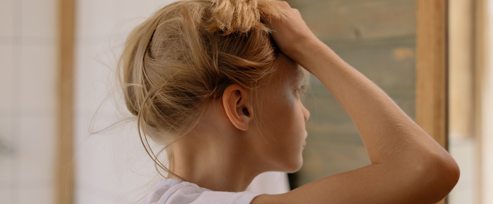 Mädchen hält sich die Haare hoch und schaut in den Spiegel. Foto: Cottonbro/Pexels