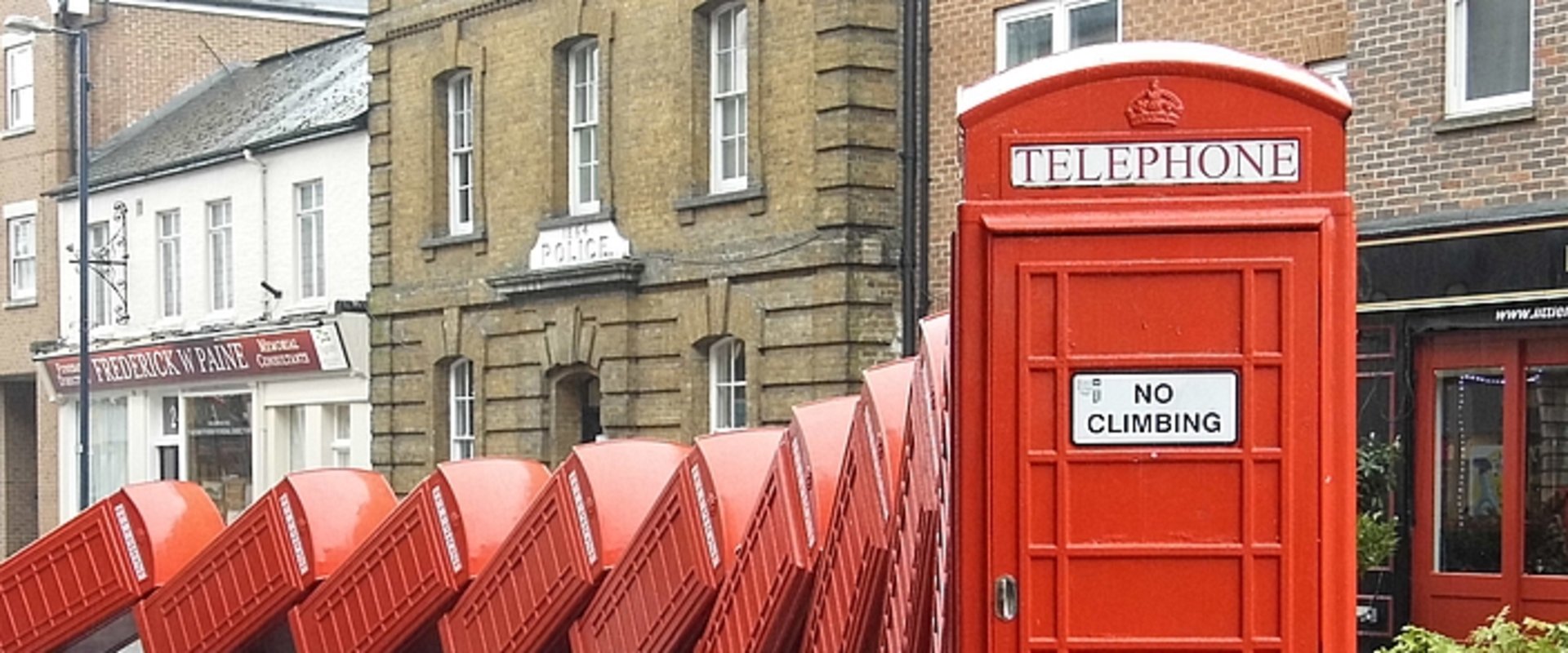 Skulptur „Out of Order“ von David Mach in Kingston upon Thames, eine Reihe rot lackierte Telefonzellen, die wie Dominosteine ineinander fallen. Foto: Kingston upon Thames