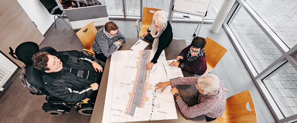 Mitglieder sitzen am Tisch über einem Bauplan.