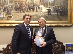 Oberbürgermeister Jürgen Krogmann und Bürgermeister Peter den Oudsten, im Hintergrund ein großes Ölgemälde. Den Oudsten hält ein in Folie verpacktes Geschenk. Foto: Stadt Oldenburg