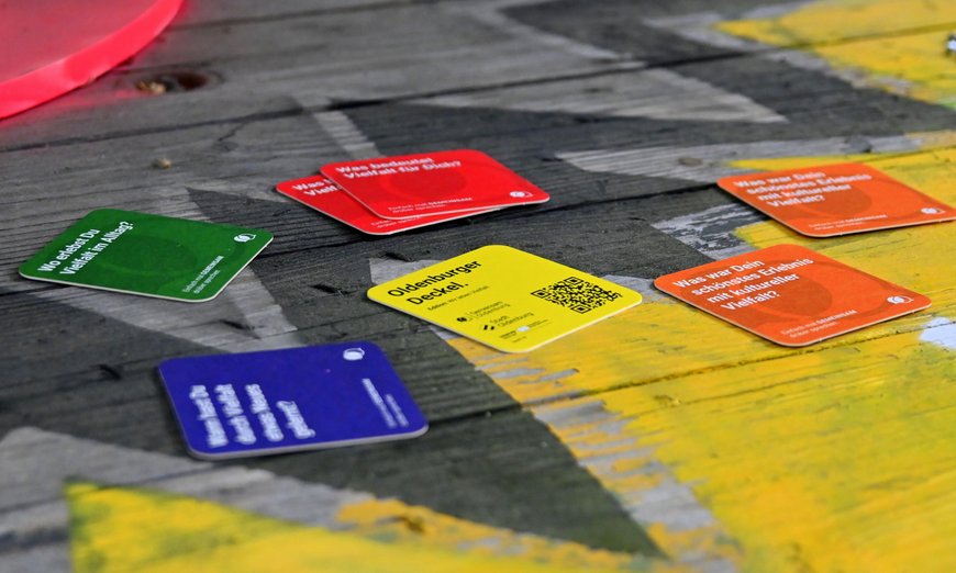 Auf einem Holztisch liegen bunte Karten in Form von Bierdeckeln. Foto: Robert Gertzen