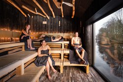 Vier Personen entspannen in der Flusssauna im OLantis und genießen beim Schwitzen den Ausblick aufs kühle Nass. Foto: Thomas Weber