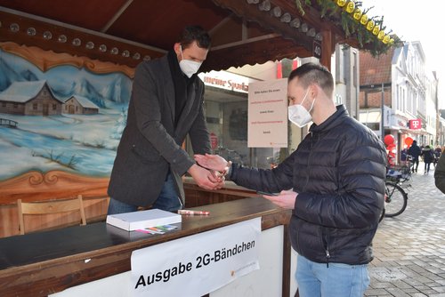 Innenstadtmanager Steffen Trawinski (links) legt Fabian Köster von der Stadtverwaltung ein Dauerbändchen ums Handgelenk, das ab dem 11. Dezember als 2G-Nachweis im Oldenburger Einzelhandel gilt. Foto: Stadt Oldenburg