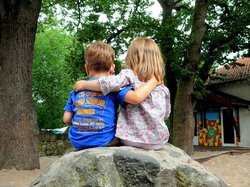 Zwei Kinder sitzen Arm in Arm auf einem Stein. Foto: S.v.Gehren/pixelio.de