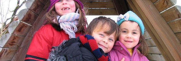 Drei Kinder stehen vor einer Holzhütte. Foto: adel/pixelio.de
