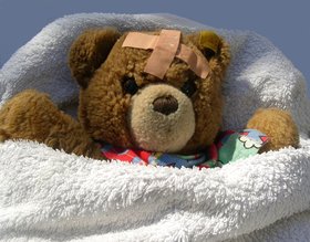 Kranker Teddy mit Pflaster liegt im Bett. Foto: S. Hofschlaeger/Pixelio