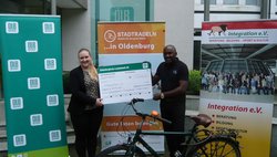 Franziska Stiebeiner, Unternehmenskommunikation Oldenburgische Landesbank AG, übergibt den Scheck für das Erreichen des siebten Etappenziels an Cyrille Lobe Ndoumbe von Integration e.V. Foto: Stadt Oldenburg Franziska Stiebeiner, Unternehmenskommunikation Oldenburgische Landesbank AG, übergibt den Scheck für das Erreichen des siebten Etappenziels an Cyrille Lobe Ndoumbe von Integration e.V. Foto: Stadt Oldenburg