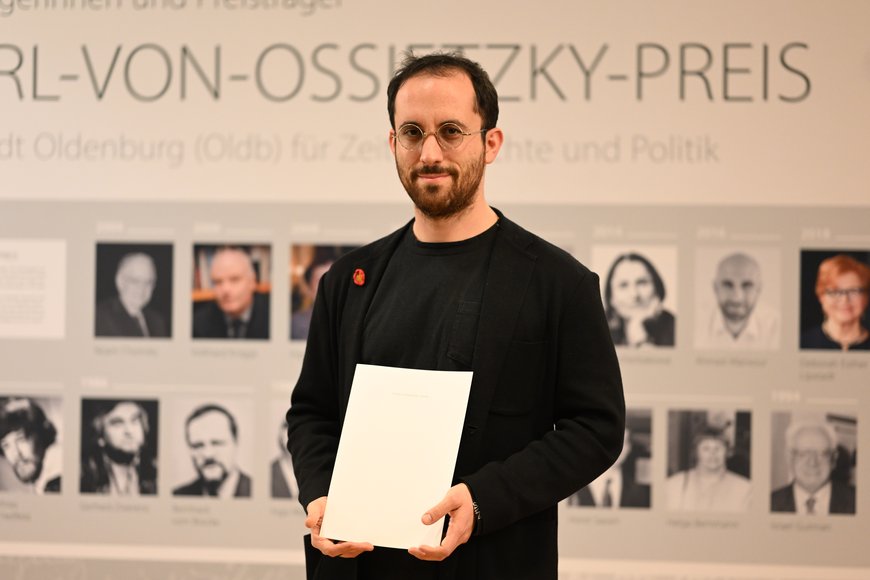 Igor Levit steht vor der Messewand der Carl-von-Ossietzky Preisträgerinnen und Preisträger. Foto: Mohssen Assanimoghaddam