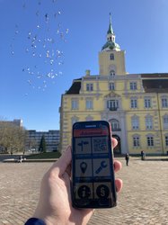 Foto von einem Handy mit der App Action Bound mit dem Oldenburger Schloss im Hintergrund. Foto: Stadt Oldenburg