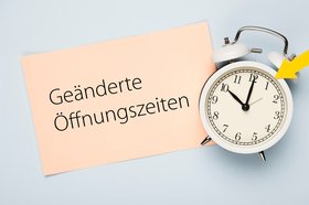 Eine analoge Uhr mit Hinweiszettel geänderte Öffnungszeiten Eine analoge Uhr mit Hinweiszettel geänderte Öffnungszeiten