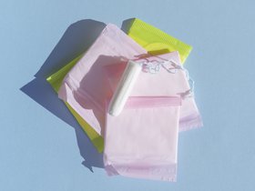 Stapel bunt verpackter Binden und darauf ein Tampon. Foto: freepik