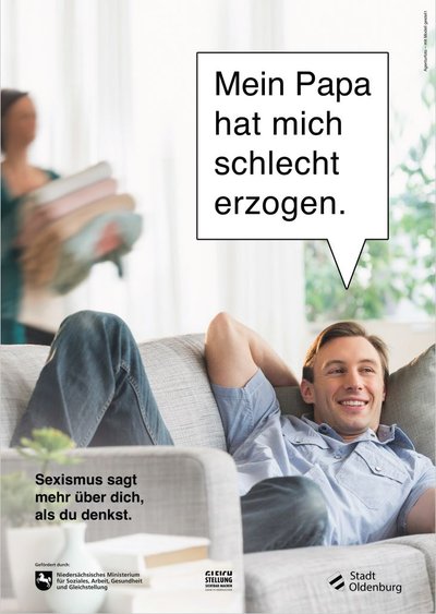Ein Mann sitzt gemütlich auf dem Sofa, während eine Frau im Hintergrund Wäsche wegräumt. Eine Sprechblase legt ihm die Worte in den Mund „Mein Papa hat mich schlecht erzogen“. Links unten steht „Sexismus sagt mehr über dich, als du denkst.“ Grafik: thjnk/Stadt Oldenburg